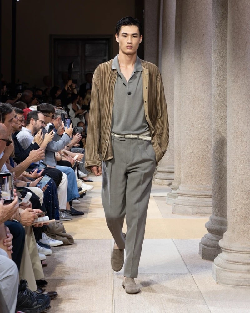 Model wears a ribbed long-sleeve cardigan with a contrasted suede front layered over a soft polo, paired with pleated tailored trousers