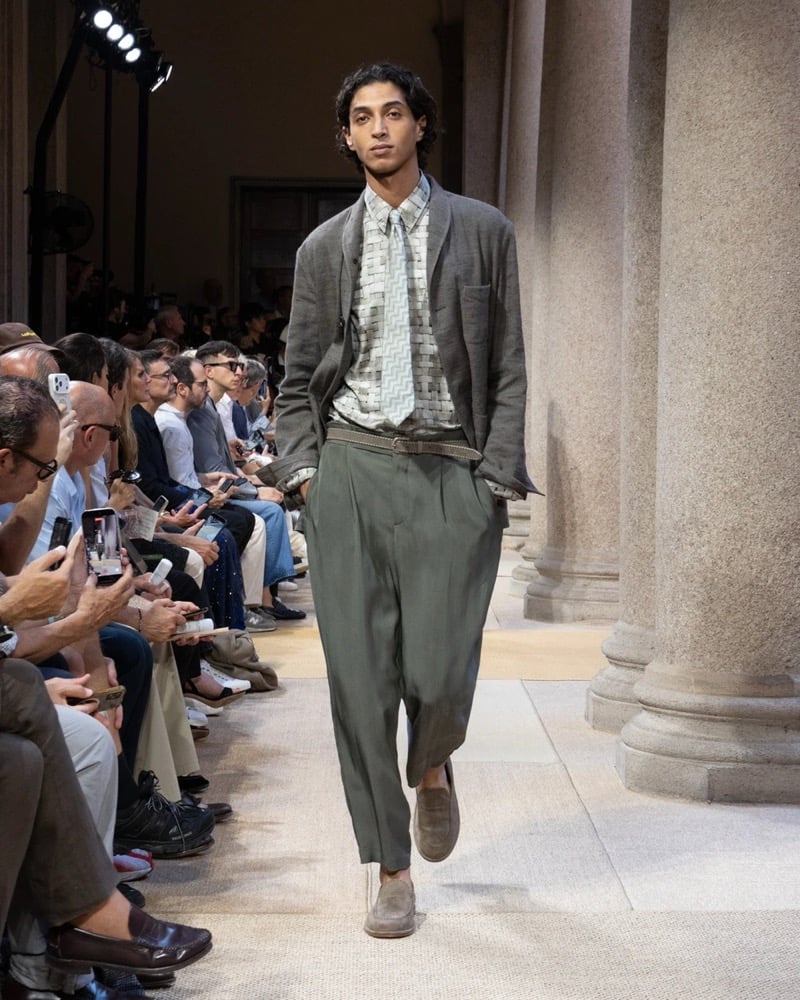Model wears a soft linen blazer with notch lapels and a chest welt pocket, layered over a geometric-print shirt and tie with wide pleated trousers