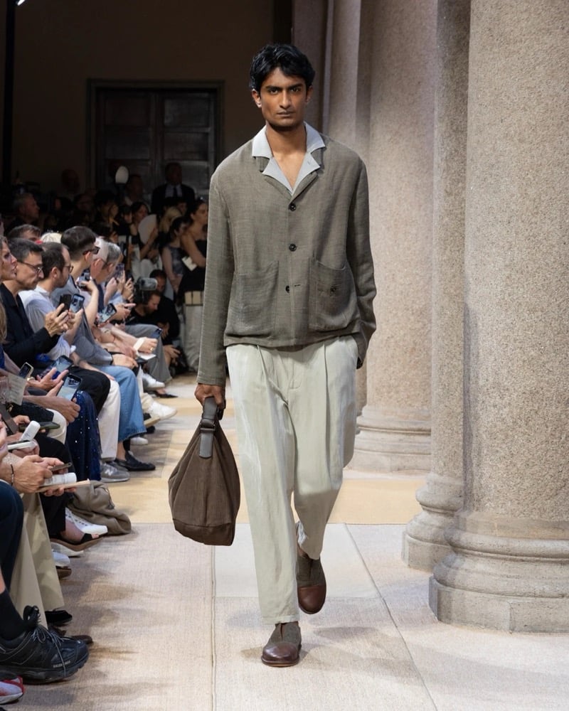 Model wears a textured linen blazer with a single button, layered over a soft shirt with wide pleated drawstring linen trousers