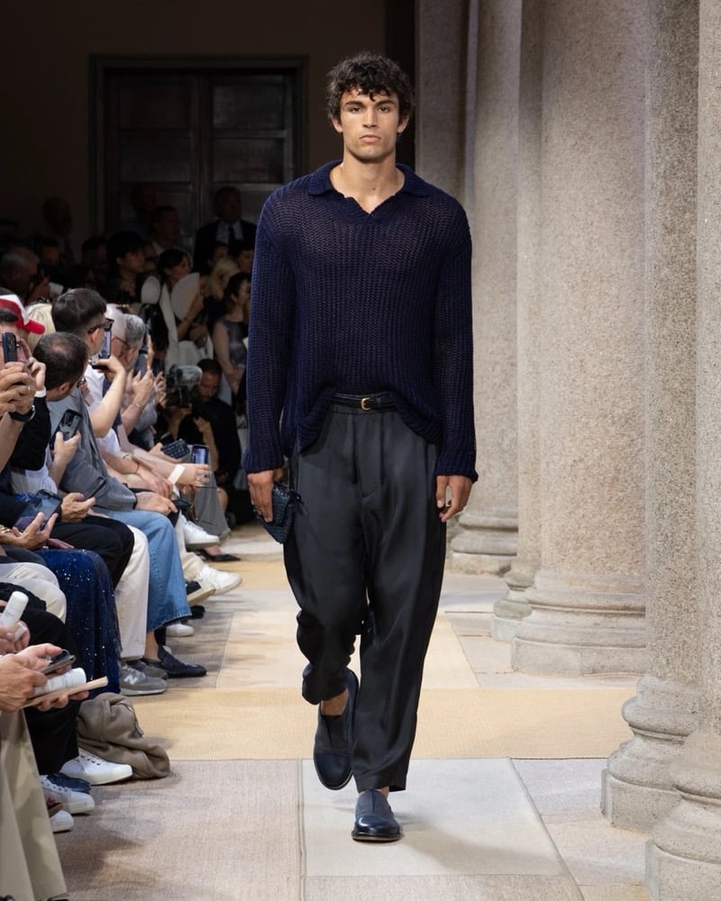 Model wears an oversized open-knit long-sleeve polo with ribbed trims, paired with wide pleated silk trousers