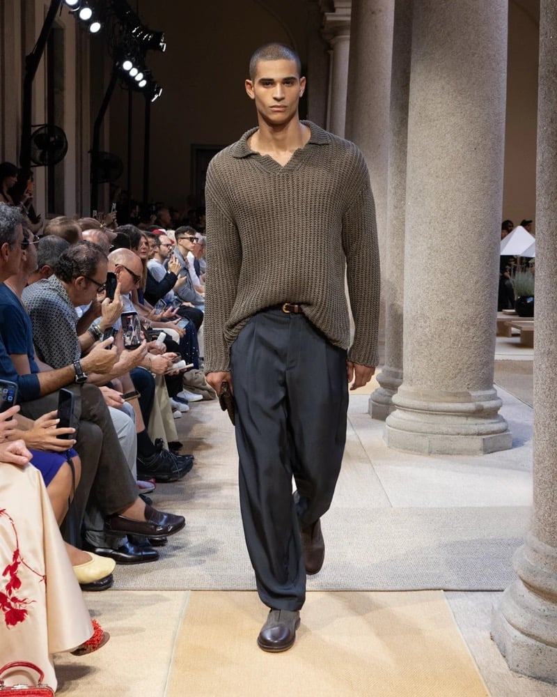 Model wears an oversized chunky open-knit V-neck pullover with ribbed trims, paired with wide pleated silk trousers