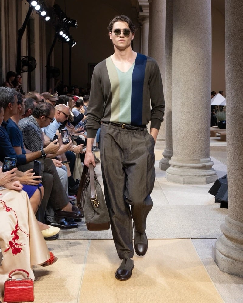 Model wears a long-sleeve V-neck knit with a vertical paneled colorblock front, paired with wide pleated linen trousers