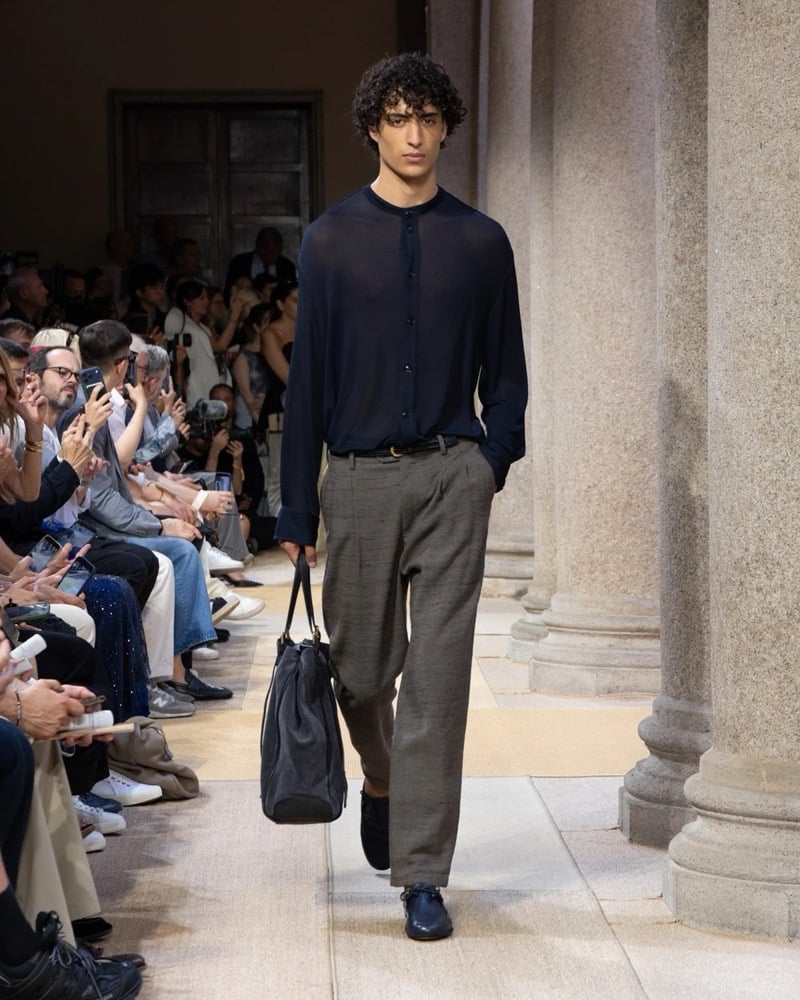 Model wears a sheer band-collar long-sleeve button-up shirt paired with wide pleated linen trousers