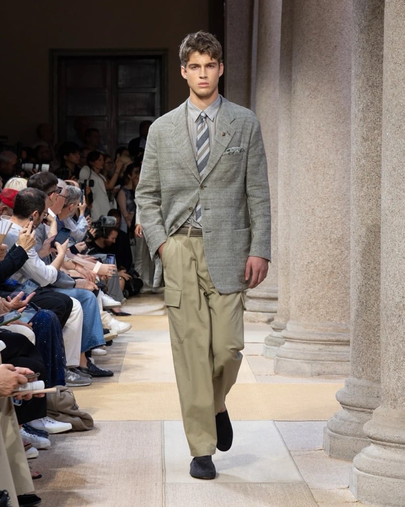 Model wears a textured linen blazer with notch lapels and patch pockets, layered over a striped shirt and tie with wide pleated cargo trousers