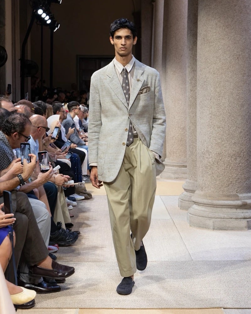 Model wears a soft linen blazer with notch lapels and patch pockets over a shirt and patterned tie, paired with wide pleated trousers
