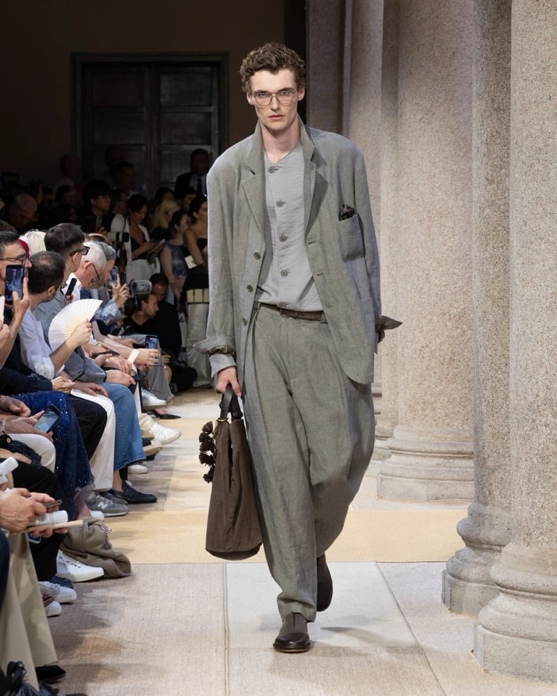 Model wears a soft single-breasted linen blazer layered over a buttoned cardigan and tee, paired with wide pleated drawstring linen trousers