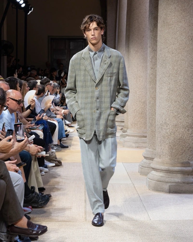 Model wears an oversized windowpane linen blazer with notch lapels and patch pockets over an open shirt, paired with wide pleated linen trousers