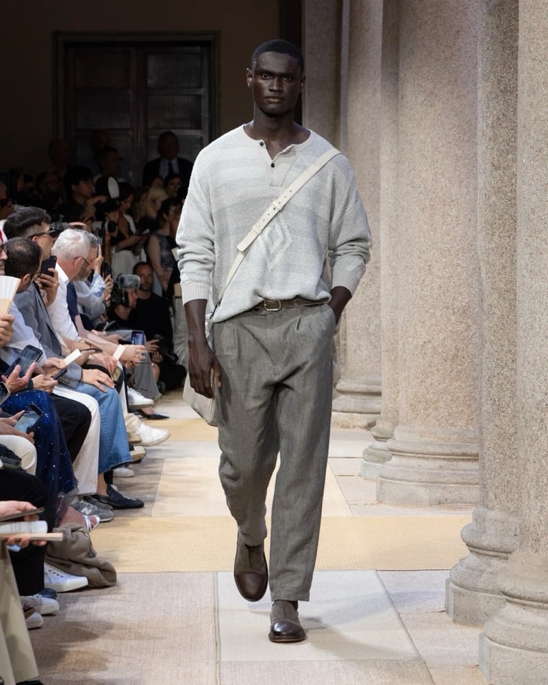 Model wears a fine-knit henley pullover with horizontal striping at the chest, paired with wide pleated linen trousers