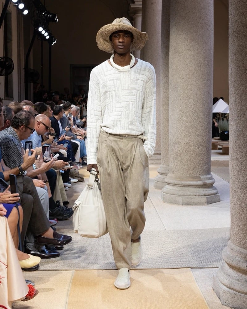 Model wears a long-sleeve open-knit patchwork pullover with a turtleneck collar, paired with wide pleated drawstring linen trousers