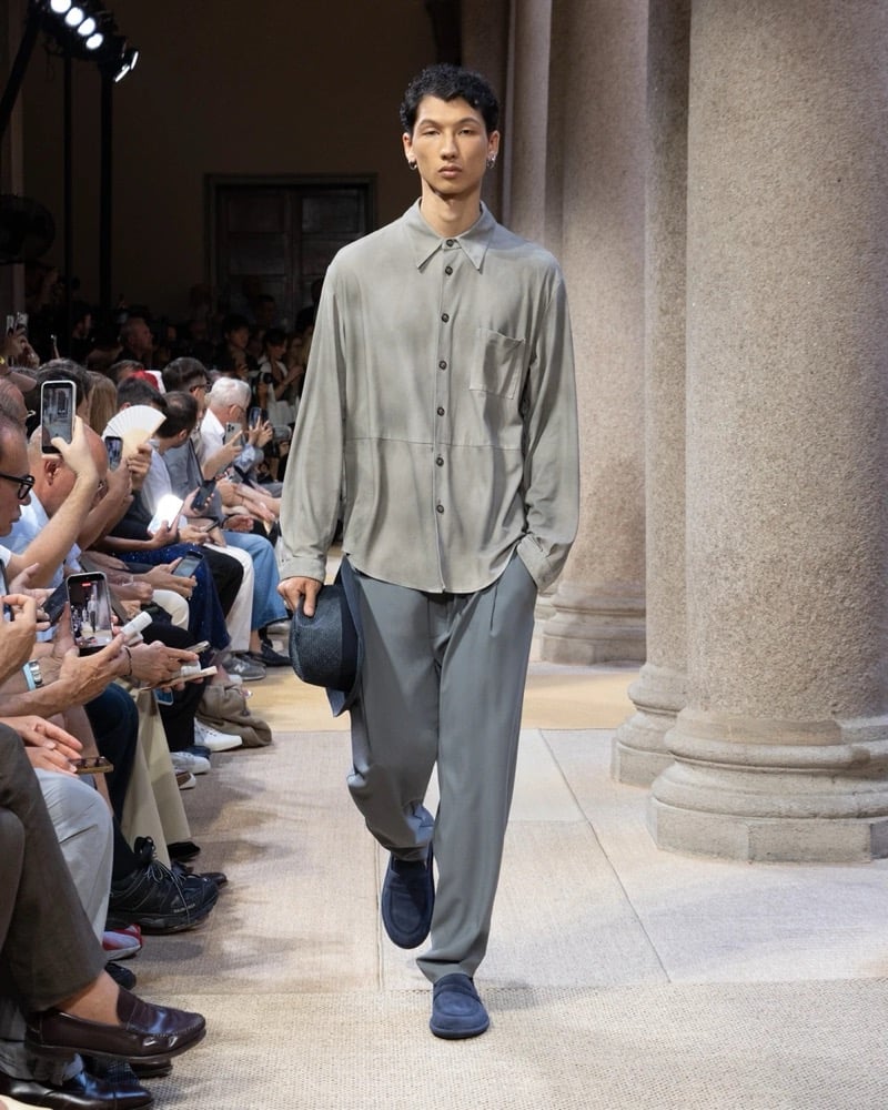Model wears an oversized long-sleeve button-up shirt with a chest patch pocket and panel seaming, paired with wide pleated silk trousers
