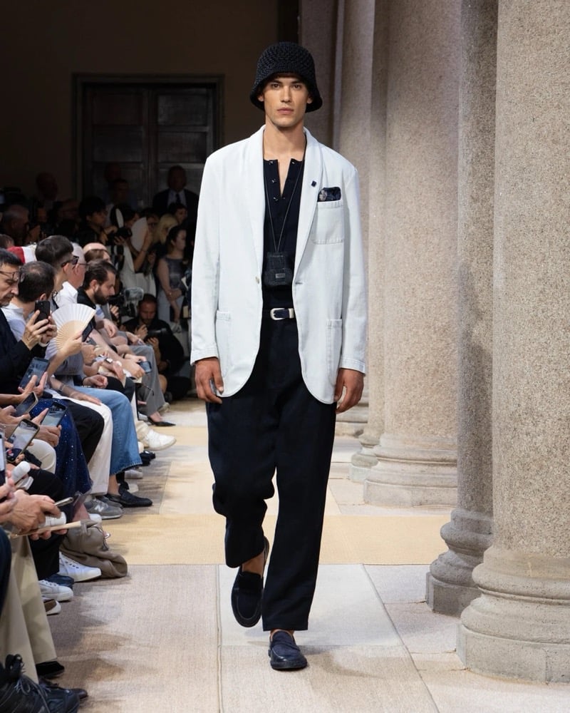 Model wears a relaxed single-breasted linen blazer with notch lapels and patch pockets layered over a henley with wide pleated linen trousers