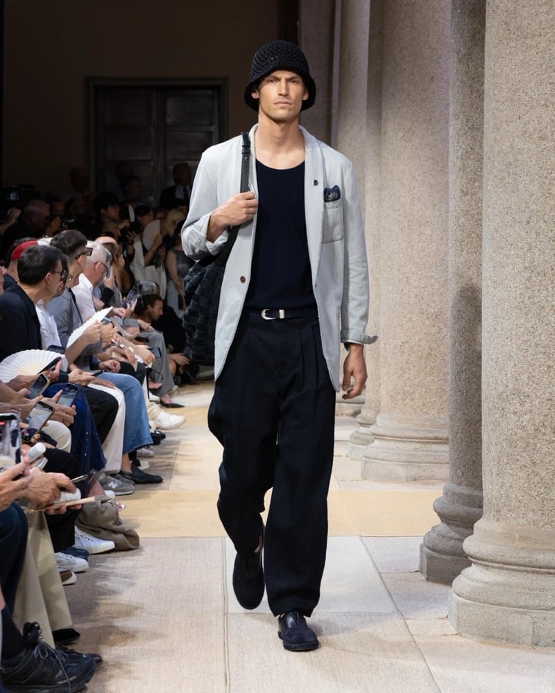 Model wears a soft single-breasted linen blazer layered over a sleeveless ribbed tank, paired with wide pleated linen trousers