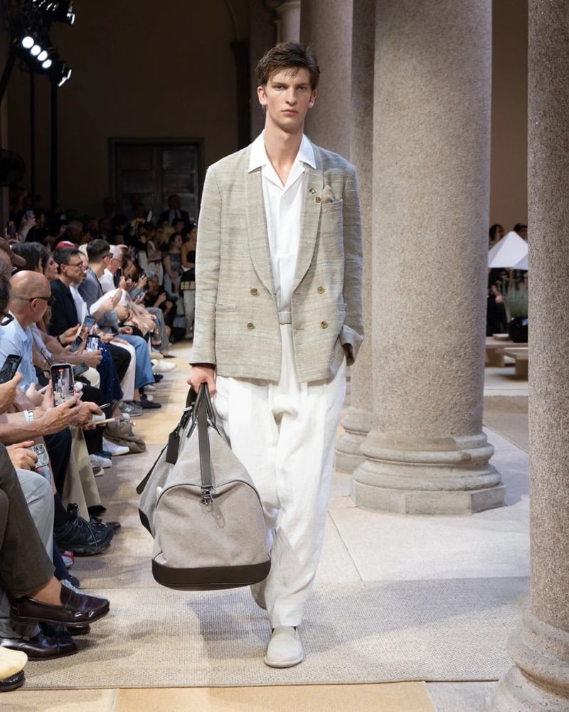 Model wears a double-breasted textured linen blazer with patch pockets over an open camp-collar shirt, paired with wide pleated linen trousers