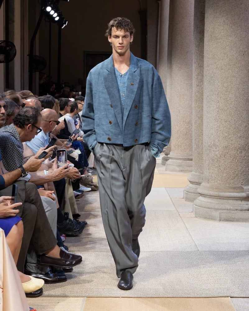 Model wears a cropped double-breasted linen blazer with peak lapels layered over a soft shirt, paired with wide pleated silk trousers