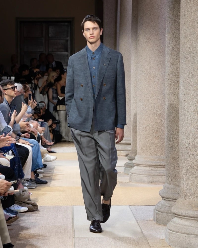Model wears a double-breasted linen blazer with notch lapels layered over a denim-style shirt, paired with wide pleated silk trousers