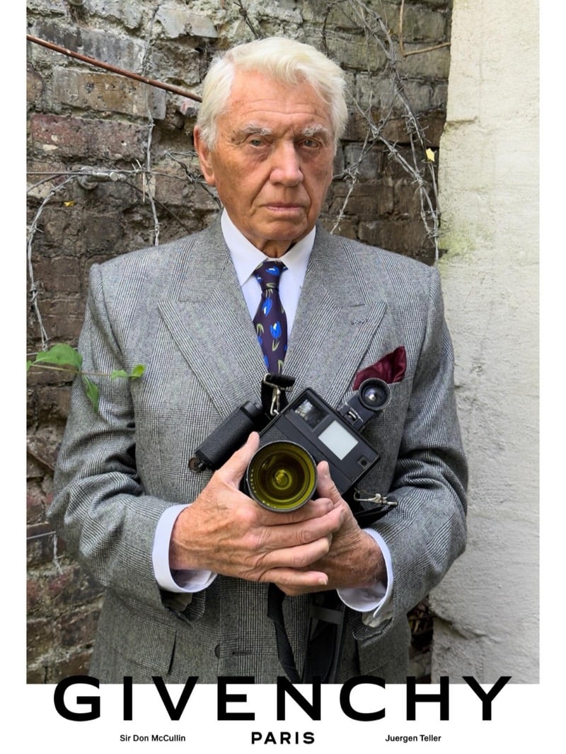 Sir Don McCullin holds a vintage rangefinder camera in a Givenchy glen check suit with a patterned silk tie and burgundy pocket square