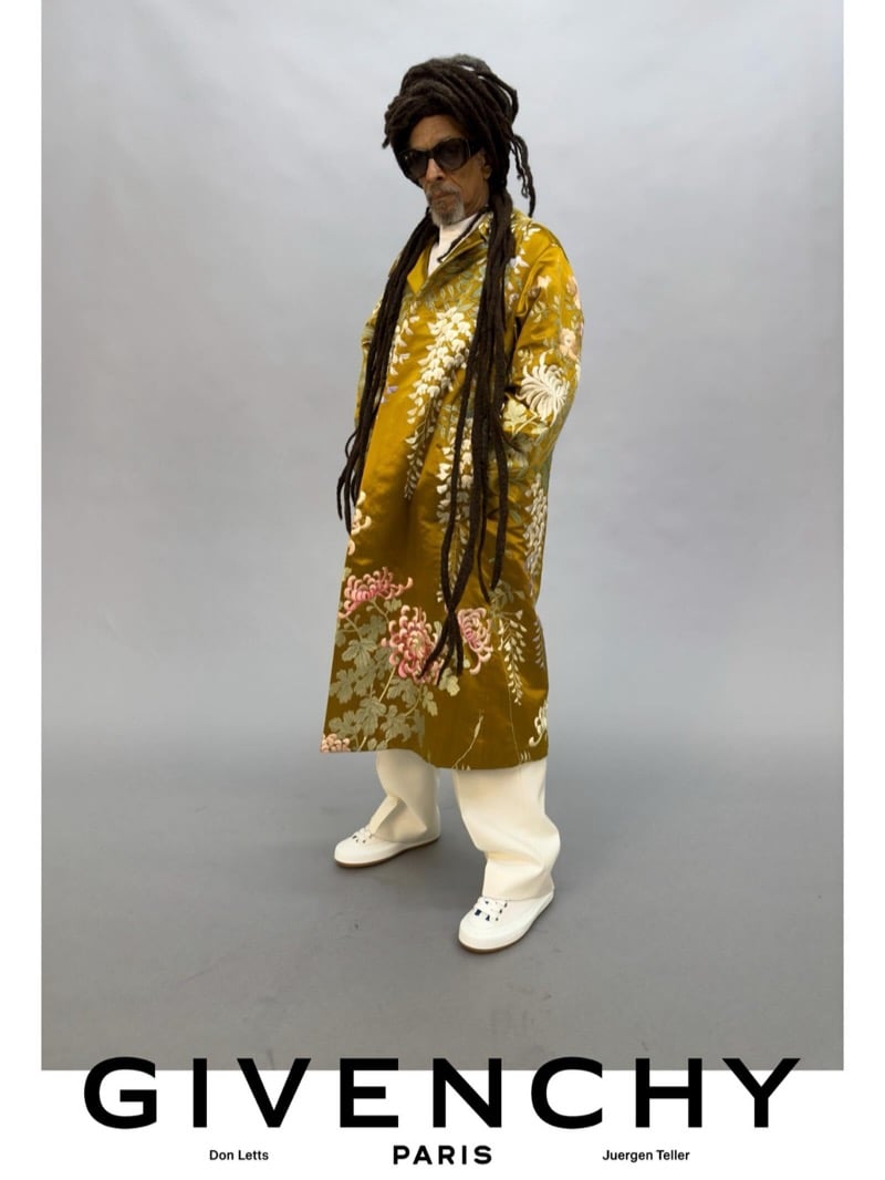Don Letts poses in a Givenchy floral-embroidered ochre brocade coat layered over white wide-leg trousers and white leather sneakers