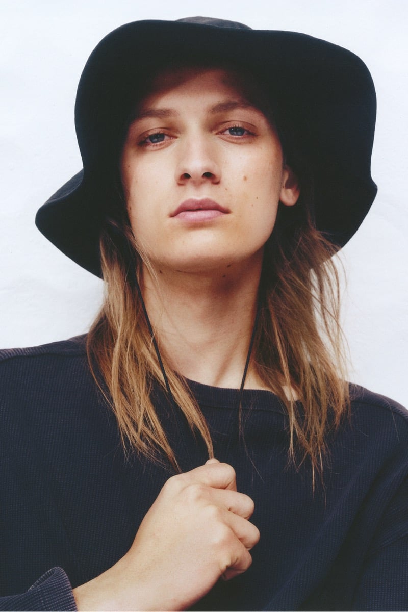 Close-up of Jesse Rinderknecht in a dark wide-brim chin-cord bucket hat over a textured waffle-knit top