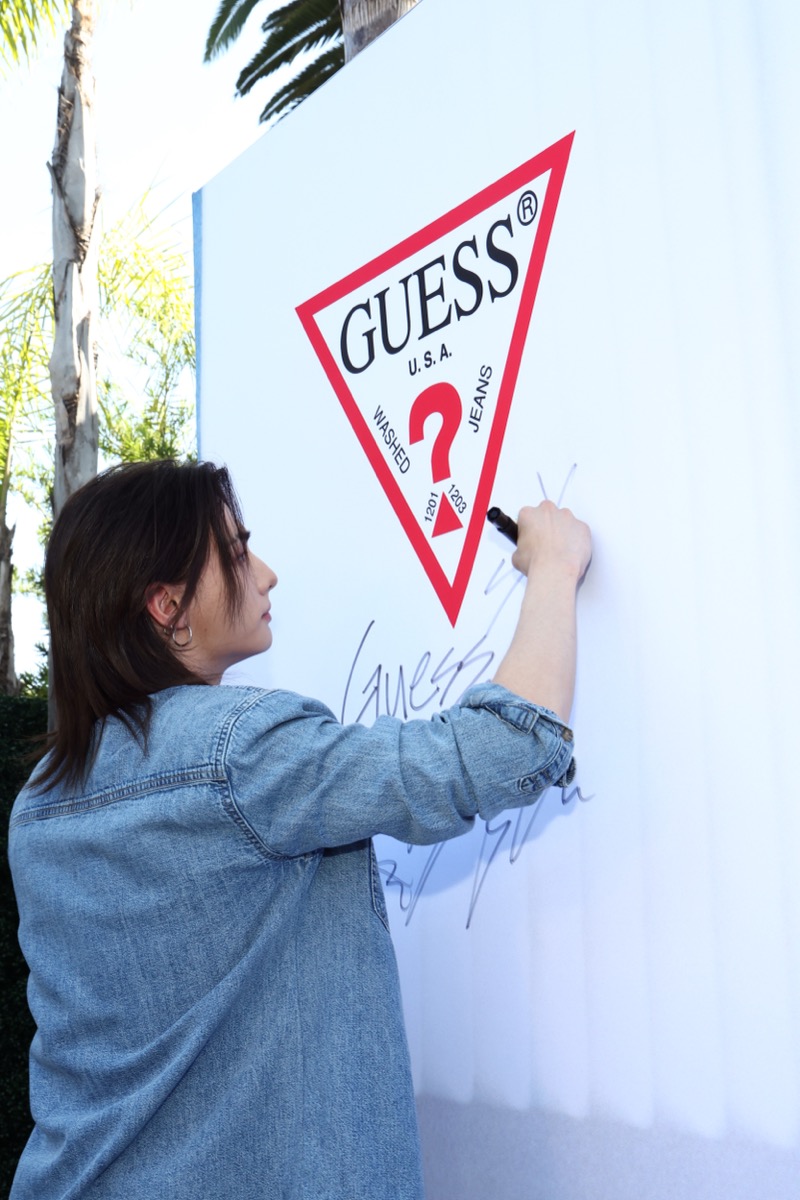 Hyunjin signing his autograph on a large white GUESS triangle logo board outside the Melrose flagship