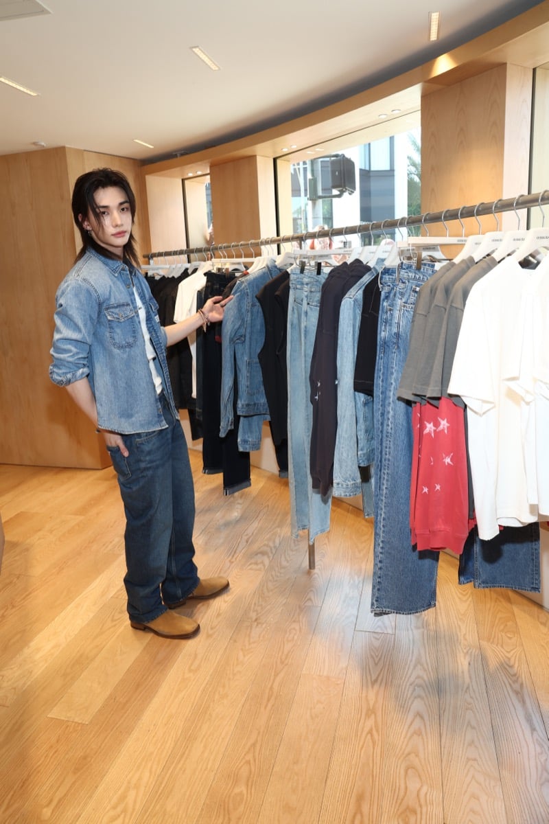 Hyunjin browsing GUESS denim racks inside the Melrose flagship in a blue denim shirt and matching jeans with tan suede boots
