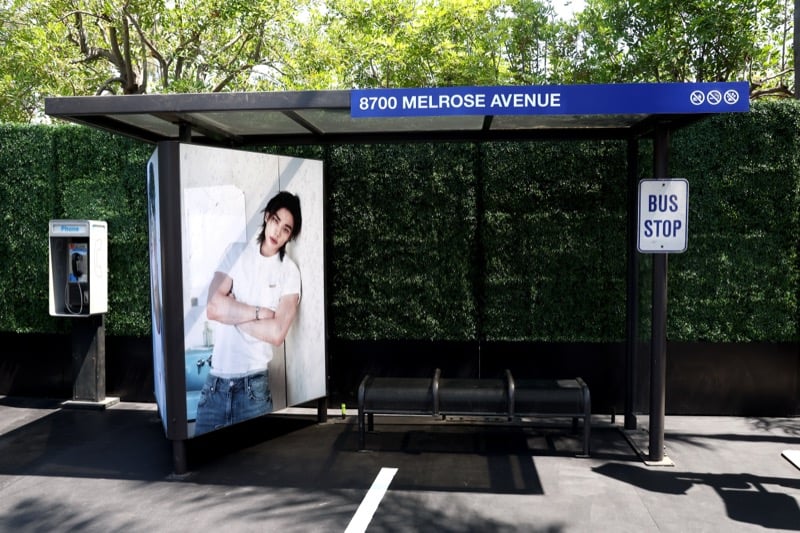 GUESS bus stop installation at 8700 Melrose Avenue featuring a large Hyunjin campaign panel and a vintage-style phone booth for fan video messages