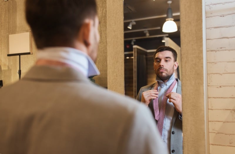 Young man tying a tie in front of a mirror inside a menswear store