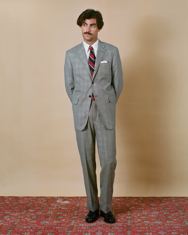 Victor Netland models the J. Press Ivy three-button suit in light gray Prince of Wales check, paired with a striped repp tie, a button-down shirt, and dark tassel loafers