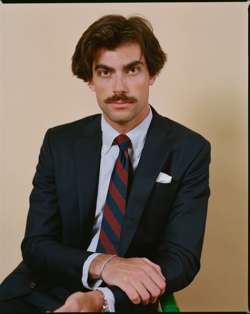 Close-up portrait of Victor Netland in a dark J. Press Ivy suit jacket worn over a striped Oxford shirt, a striped repp tie, and a pocket square