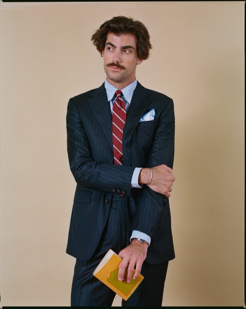 Victor Netland in the J. Press Kennedy two-button chalkstripe suit, paired with a light blue dress shirt, a burgundy striped repp tie, and a patterned pocket square