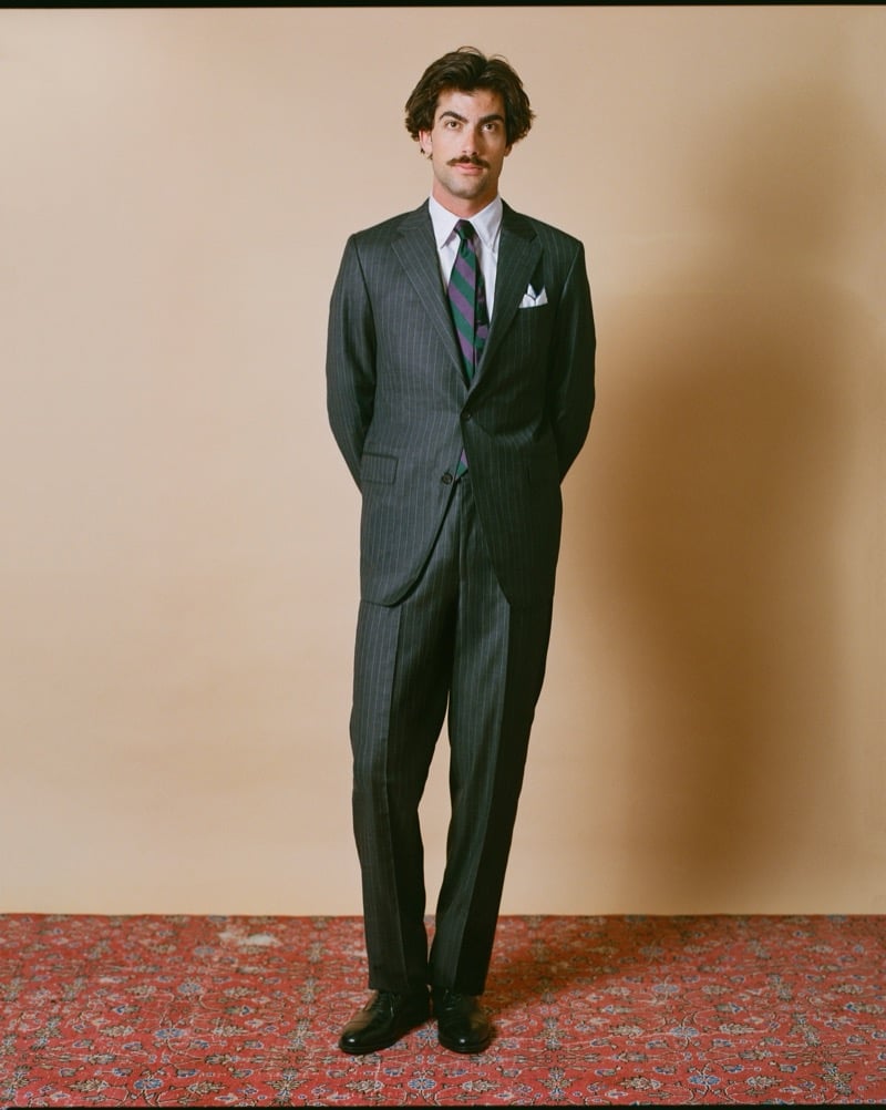 Victor Netland models the J. Press Kennedy two-button suit in charcoal chalkstripe with a dress shirt, a green and purple striped repp tie, and dark derby shoes