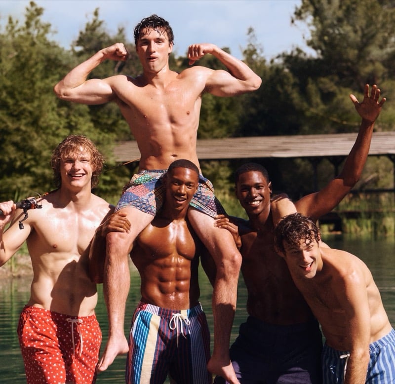 Models Anthony Foster, Jack Lumsden, Ebeneze Brown, Ronald Epps, and Conor Fay shirtless by the lake in J.Crew Camp Crew summer 2026 swim trunks, with Jack Lumsden lifted onto Ebeneze Brown's shoulders flexing both arms