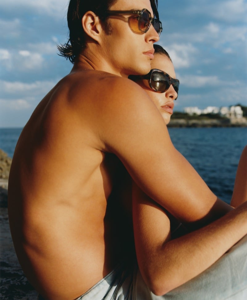 A man and woman embrace by the sea wearing Jimmy Fairly's The Eloi and The Aela sunglasses with amber and brown tinted lenses