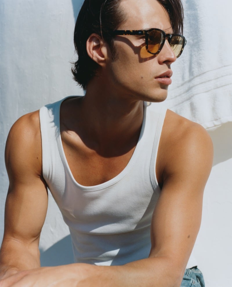 Louis Baines wears Jimmy Fairly's The Headlight yellow tortoiseshell sunglasses with amber lenses and a white ribbed tank top against a sun-washed white wall