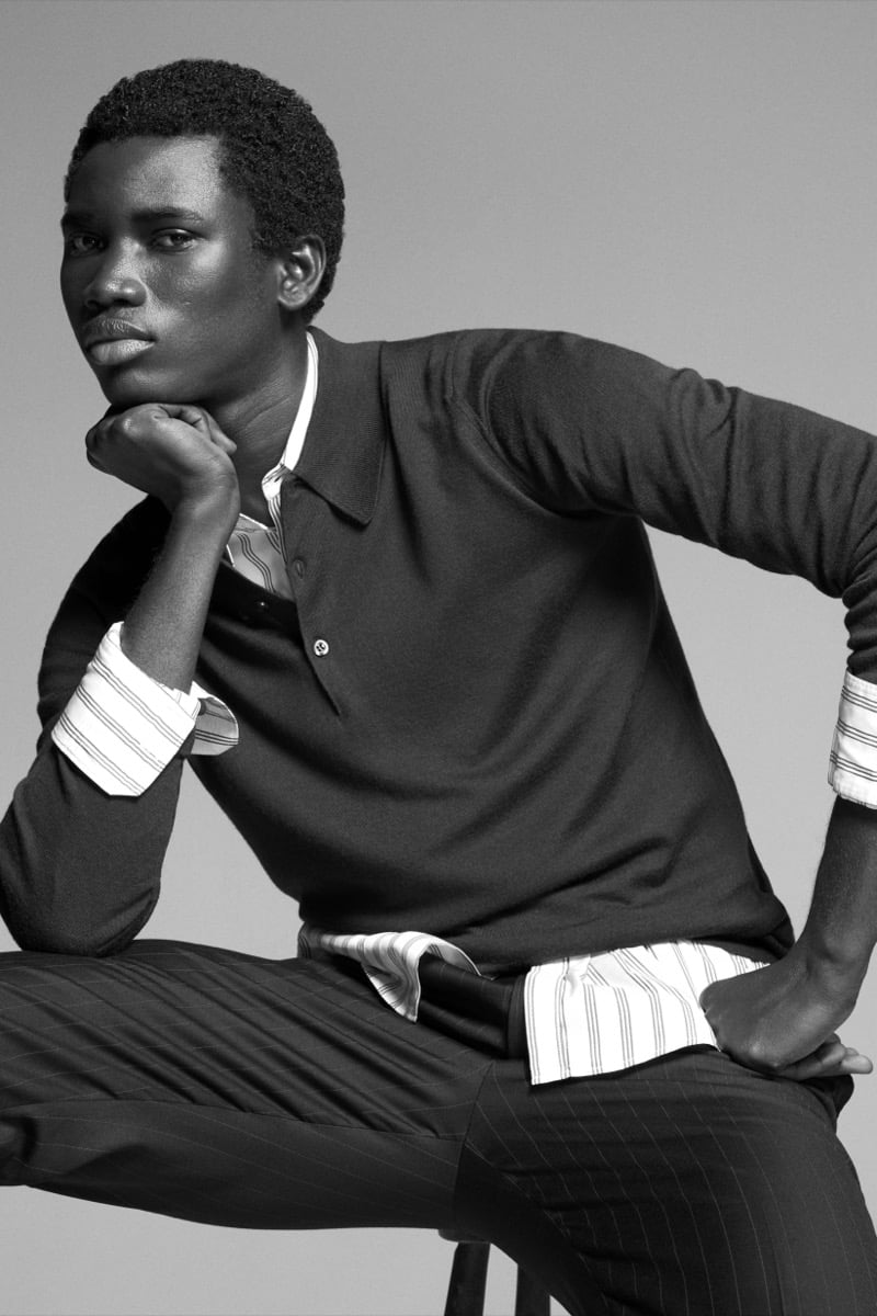 Alexander Acquah models the John Smedley Finchley Sea Island cotton long-sleeve polo, layered over a striped shirt with chalkstripe trousers