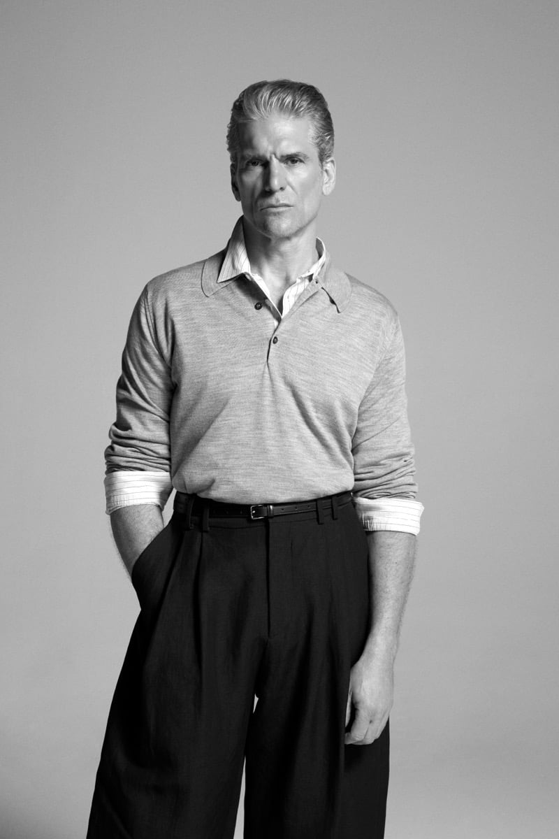 Felix Friedman wears the John Smedley Finchley long-sleeve polo in a heathered shade, layered over a striped shirt with dark pleated wide-leg trousers