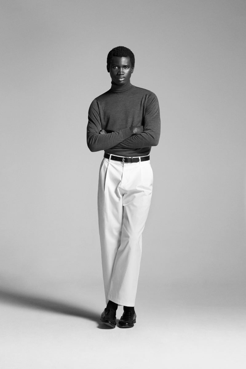 Alexander Acquah crosses his arms in the John Smedley Hawley Sea Island cotton roll neck, paired with pleated trousers and dark loafers