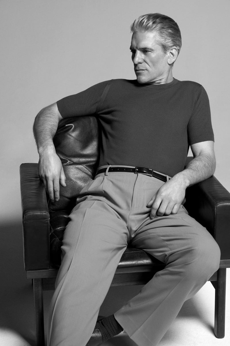 Felix Friedman lounges in a leather chair wearing a John Smedley knit short-sleeve crewneck with pleated trousers for the Icons campaign