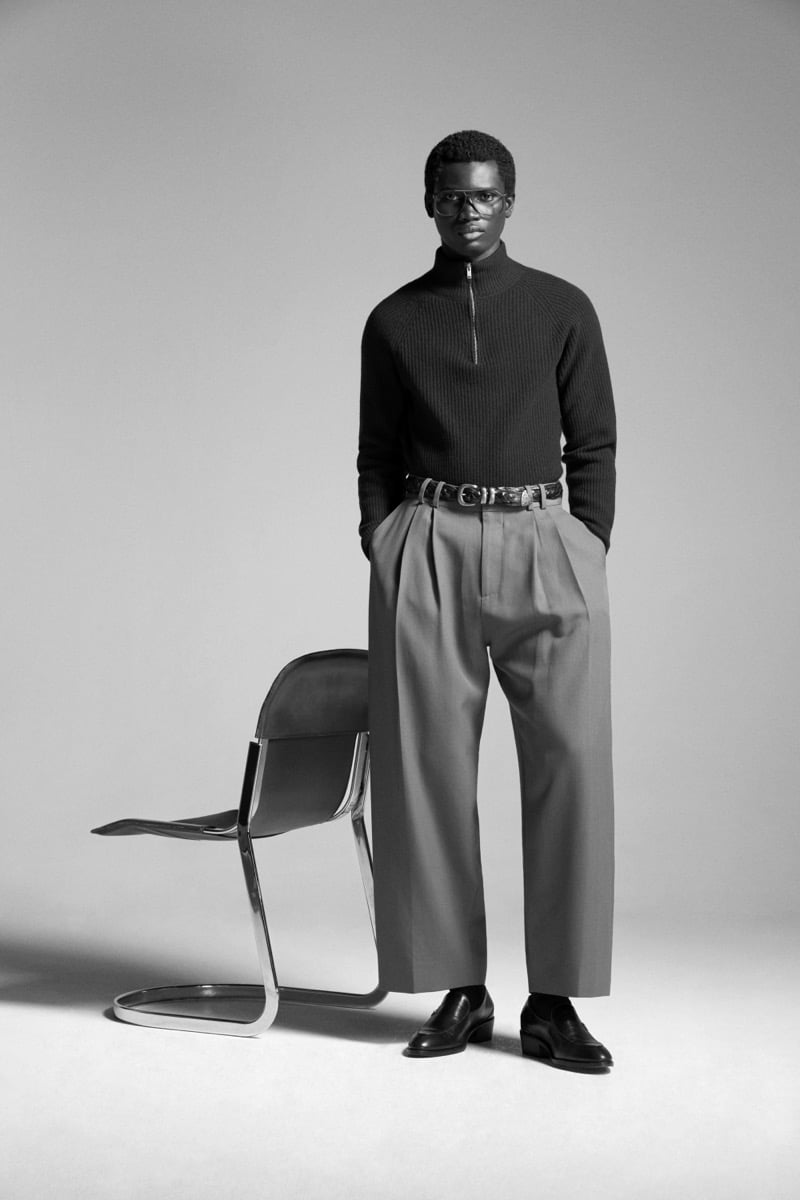 Alexander Acquah in the John Smedley Ryker eco cashmere half-zip mock neck, paired with pleated wide-leg trousers, a leather belt, and tortoise-shell glasses