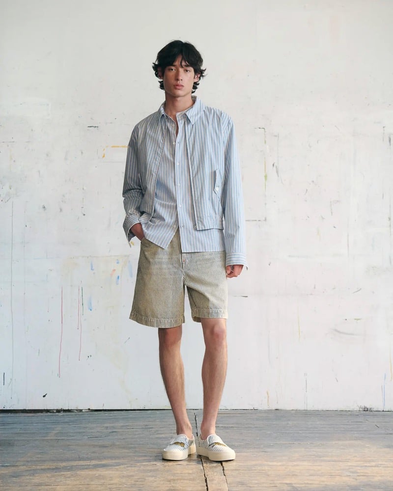 Max Fauviau wears a blue and white striped oxford shirt under a cropped striped overshirt with khaki striped shorts and white canvas platform slip-on sneakers