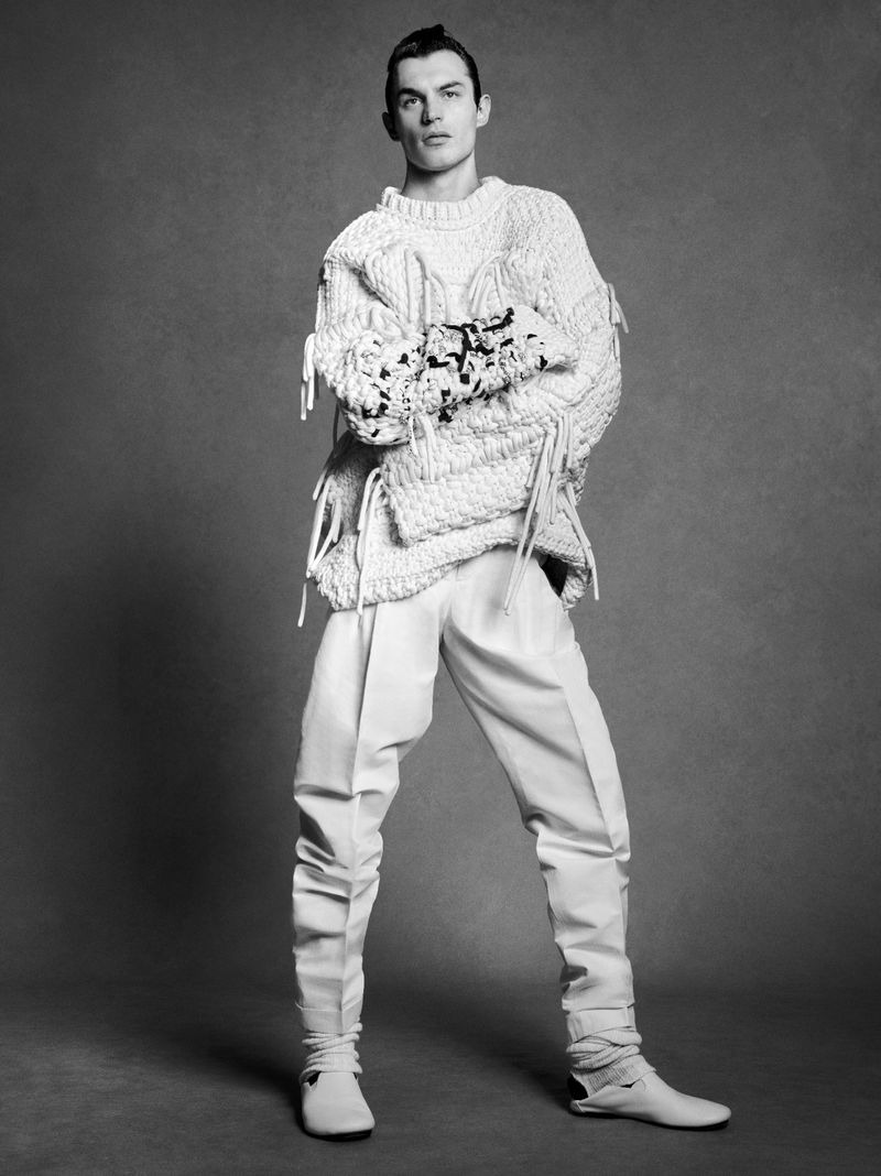 Kit Butler in an oversized cream chunky cable-knit Bottega Veneta sweater with trailing macramé fringe and beaded embroidery at the chest, off-white pleated trousers tapering into cream ankle boots