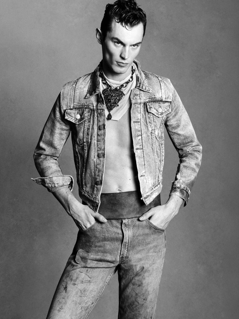 Kit Butler in a faded acid-wash cropped denim jacket with a jeweled necklace at the collar, faded mid-blue jeans, hands tucked into the front pockets, slicked-back wet hair