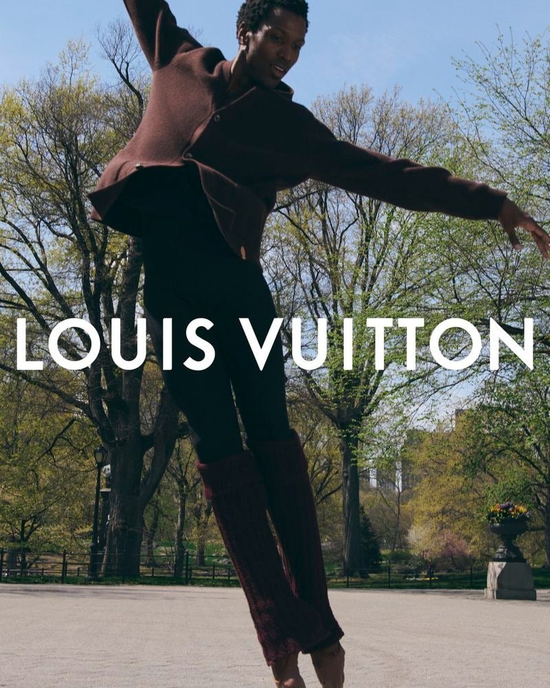 Calvin Royal III leaps with arms extended in front of Central Park trees, wearing a wool jacket, pants, and leg warmers