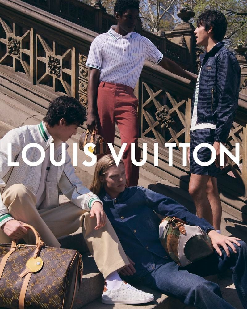 Four Louis Vuitton cast members regroup on the Bethesda Terrace steps in Central Park, with Calvin Royal III standing in a navy striped polo and rust red chinos, Luke Champion seated in an indigo denim coach jacket and matching Monogram-cuffed jeans, Mathieu Simoneau in a cream perforated leather bomber, and Akbar Shamji in a navy quilted bomber and shorts set