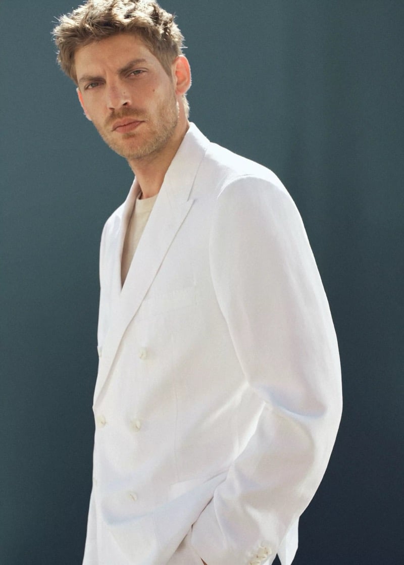 Side profile of Baptiste Radufe in a white double-breasted linen blazer layered over a cream knit tee for Mango Man summer 2026