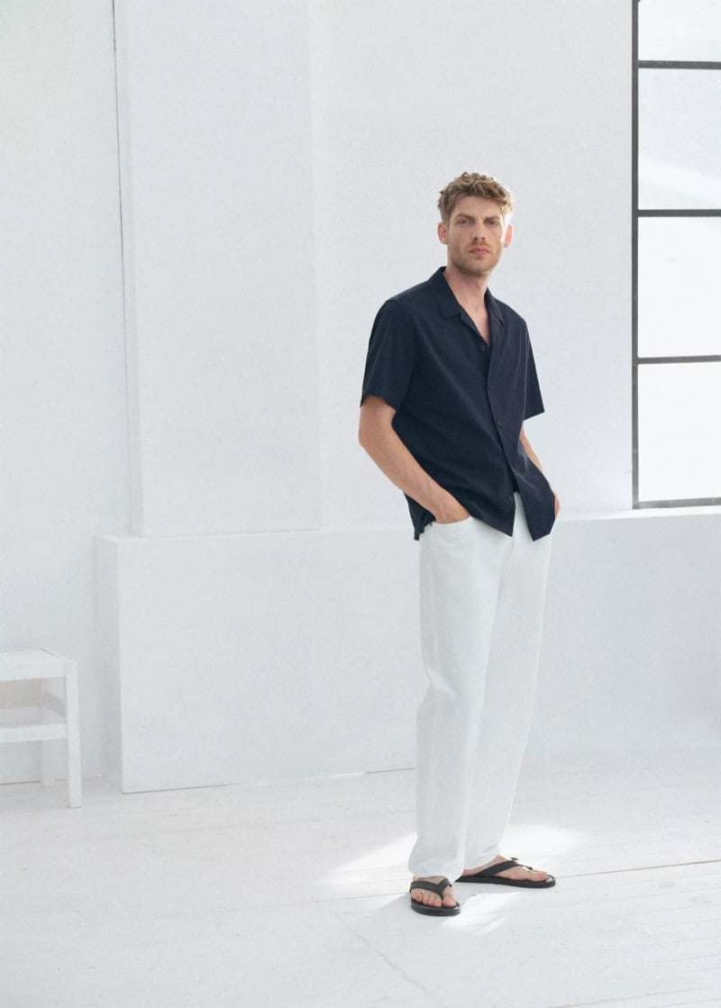 Baptiste Radufe wears a dark short-sleeve camp shirt with wide-leg white linen trousers and black flip-flop sandals for Mango Man summer 2026