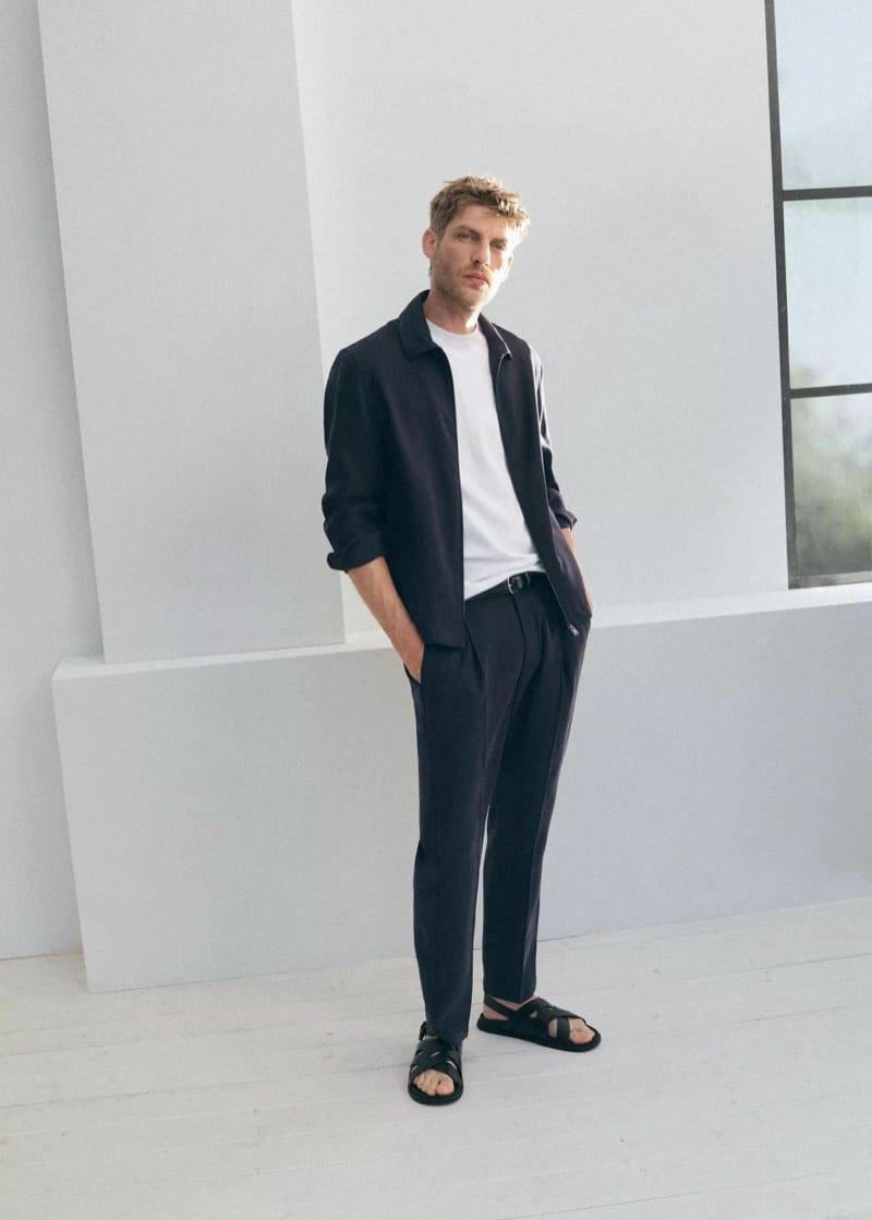 Baptiste Radufe wears a dark zip-front jacket with white T-shirt, pleated trousers with a leather belt, and black cross-strap sandals for Mango Man summer 2026