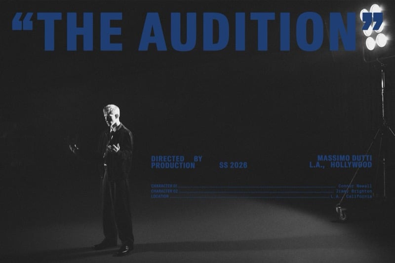 Black-and-white Massimo Dutti The Audition title card with Connor Newall standing under a single studio light in a dark suit, blue type laying out the director, production, spring-summer 2026 season, L.A. Hollywood location, and the two-character cast