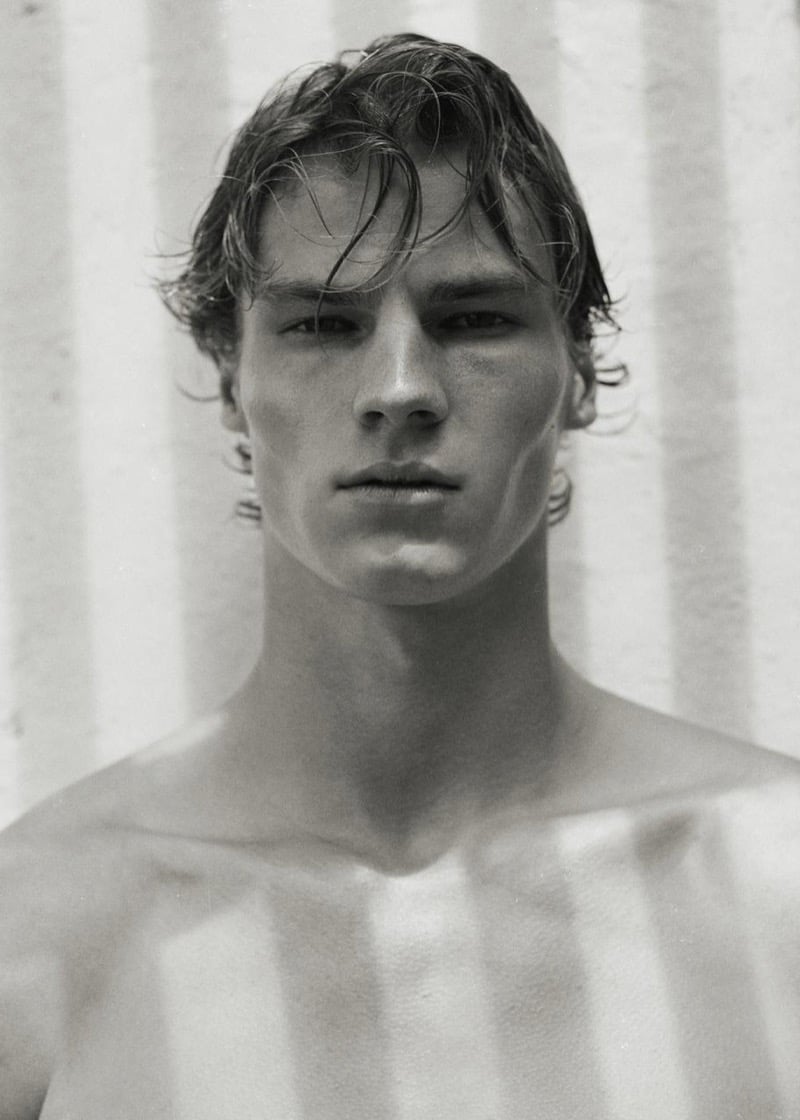 Henry Rank in a tight black-and-white portrait, shirtless against a striped curtain casting shadows across his face and chest, wet hair falling over the forehead