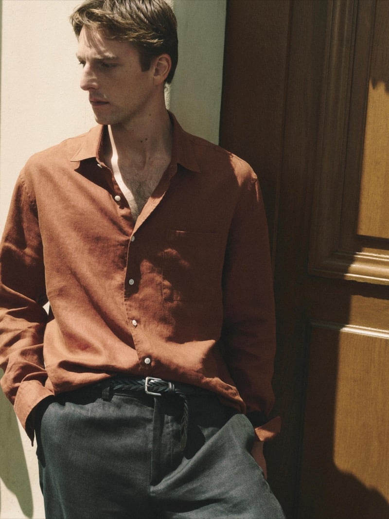 Quentin Demeester against a paneled door in a Massimo Dutti linen shirt, woven leather belt, and pleated trousers