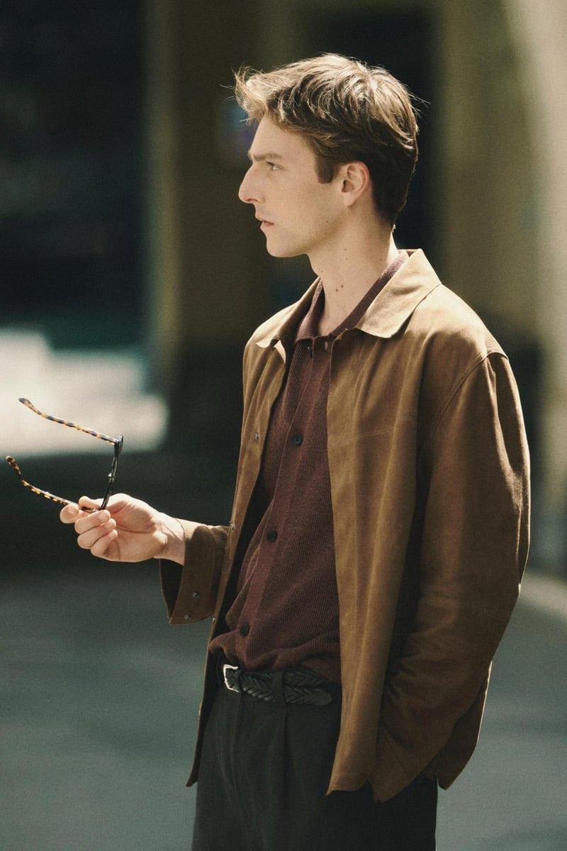 Quentin Demeester in profile holding a pair of tortoiseshell sunglasses, wearing a Massimo Dutti suede blouson over a ribbed knit polo